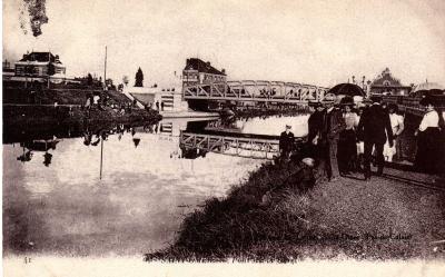 Au bord du canal, les danes avec leurs ombrelles et les messieurs en canotier. Au fond on aperçoit la passerelle qui enjambe le canal pour aller vers la gare.